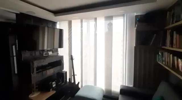 Sala de un apartamento inteligente con ventanal, persianas automatizadas y TV en la pared